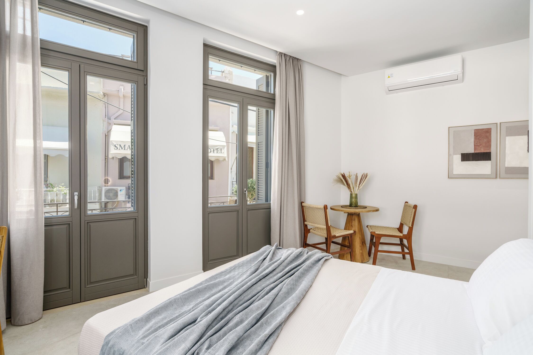 A hotel room with a bed, a small table with chairs, and a window with curtains.