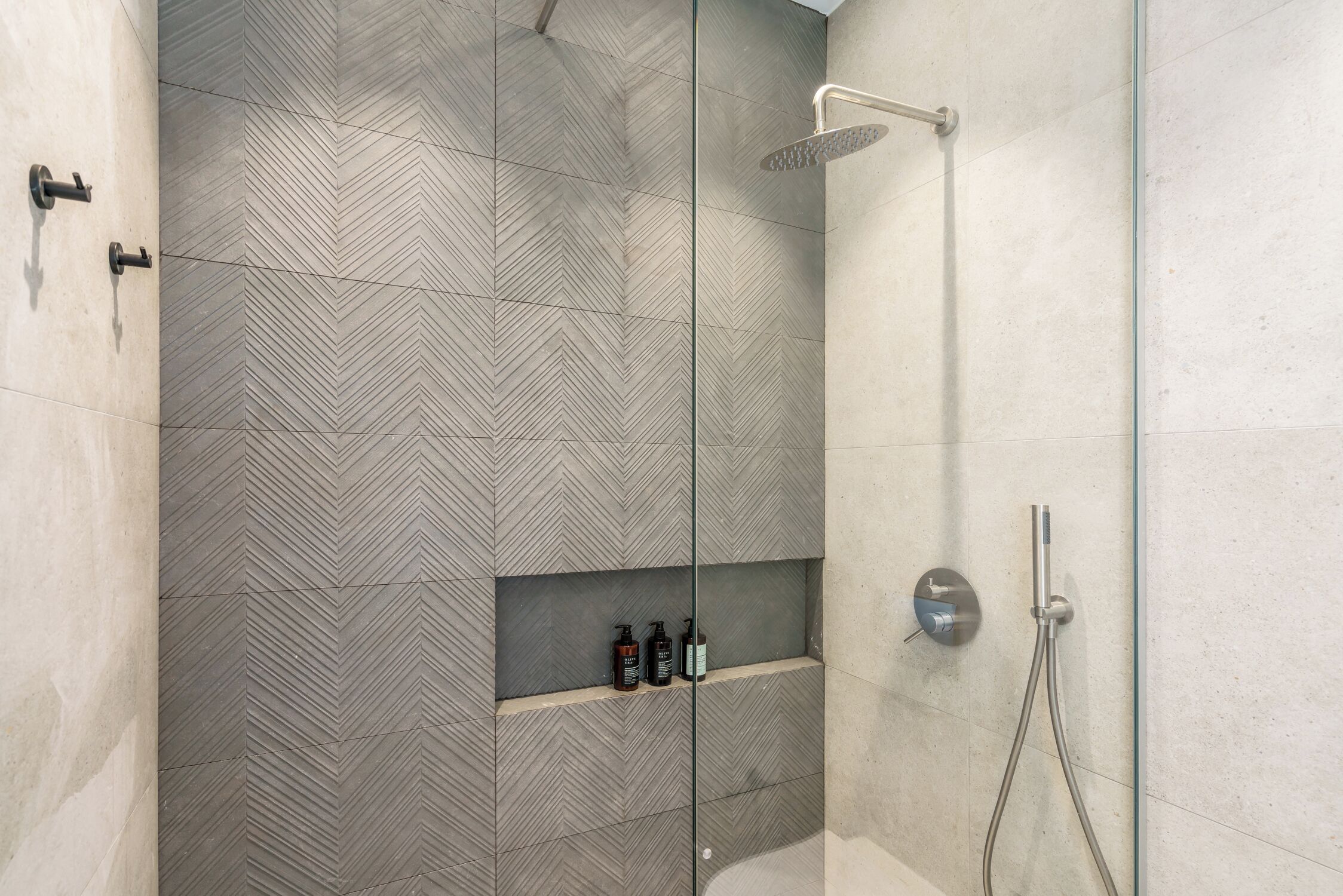 Un espace douche moderne avec un motif de carrelage en chevrons, une paroi en verre et une étagère intégrée pour les articles de toilette.