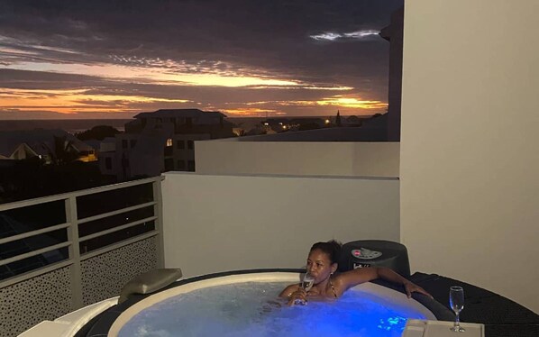 A person relaxing in a hot tub with a sunset view.