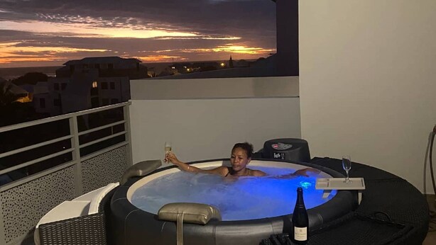 A person relaxing in a hot tub with a sunset view, a bottle of wine, and a remote control. - T4 duplex and rooftop in the heart of Saint-Pierre, this new luxury residence be (Saint-Pierre)