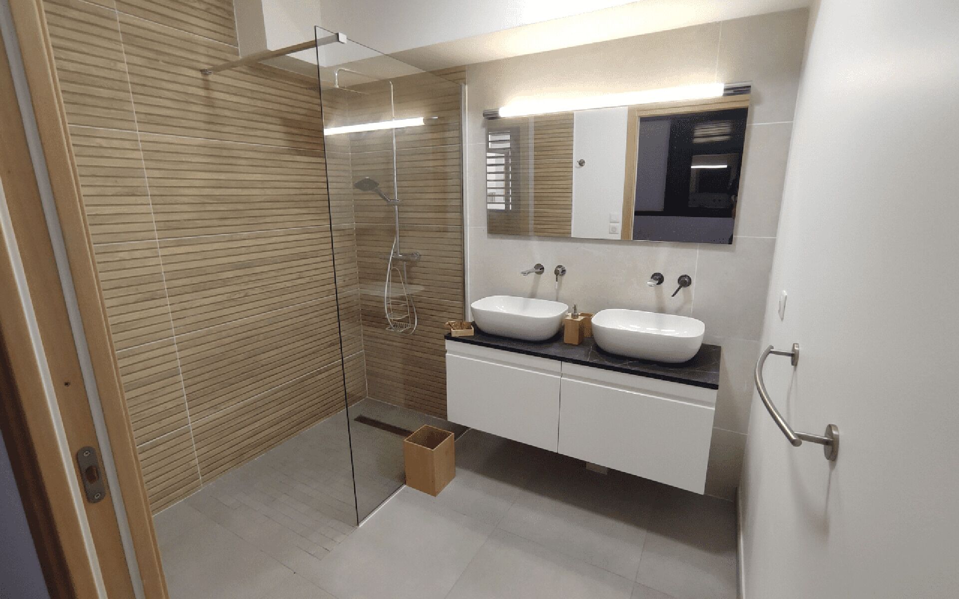 Une salle de bain moderne avec une douche à parois de verre, deux lavabos et un grand miroir.