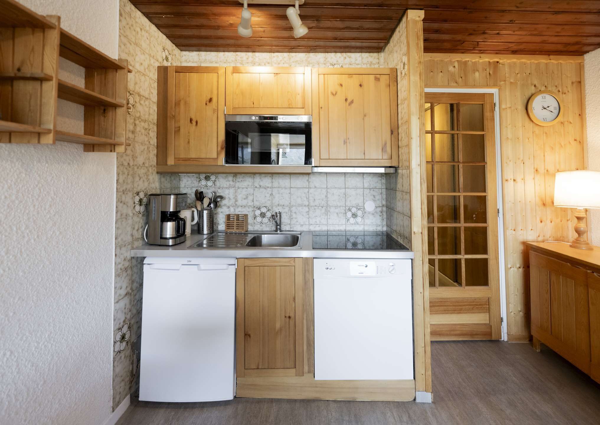 A compact kitchen with wooden cabinets, a built-in microwave, a coffee maker, and a dishwasher.