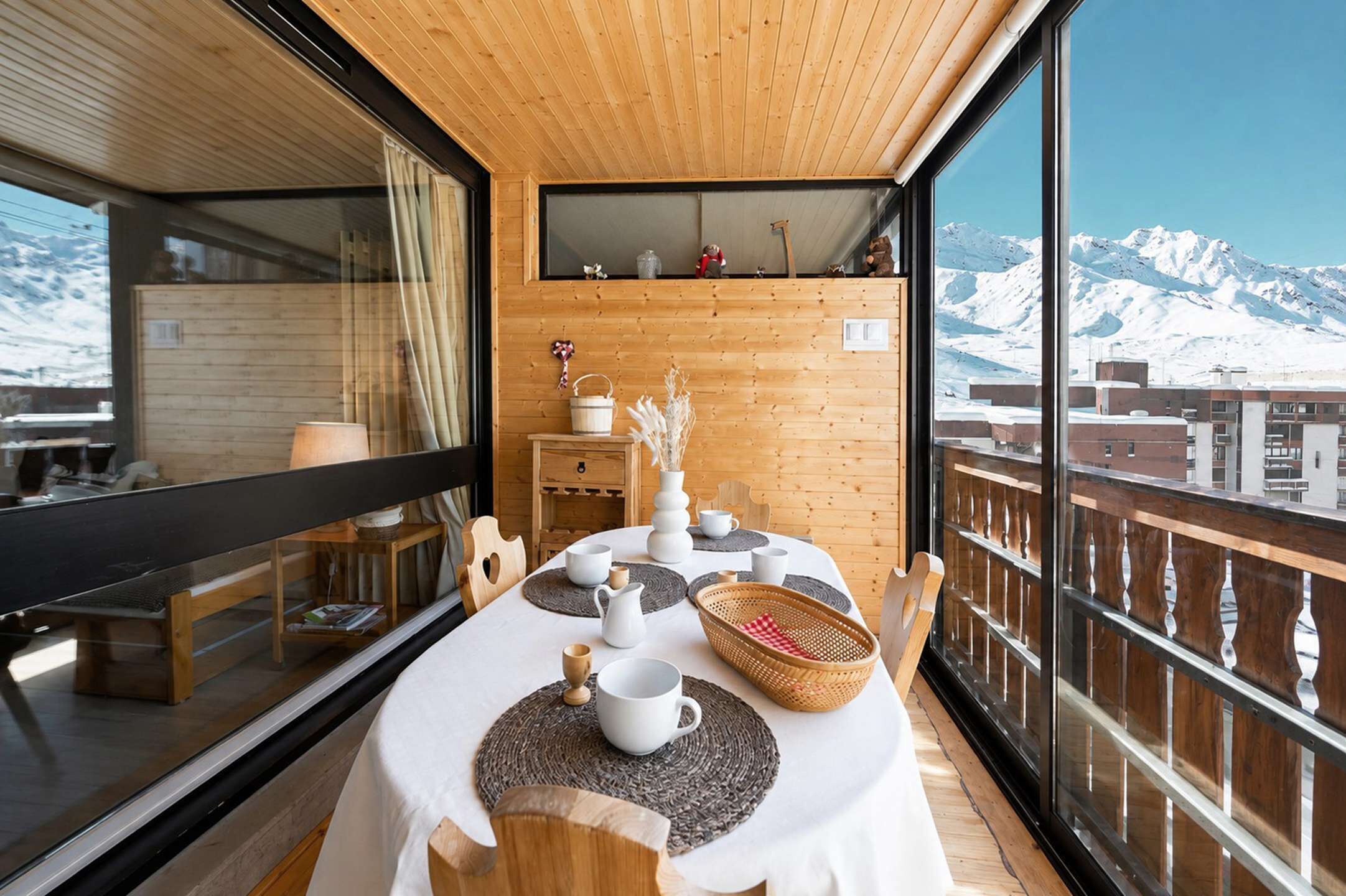 A wooden deck with a table set for dining, overlooking a snowy mountain.
