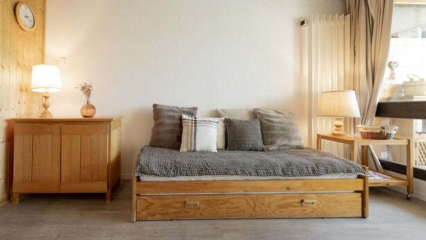 A wooden bed with a checkered bedspread, two bedside tables with lamps, and a wooden wardrobe.