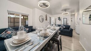 A modern dining area with a long table set for a meal, a dark blue sofa, and a ceiling fan. - 3BR 2BA Home w Jacuzzi Near Reid Park & Zoo Unit A (Tucson)