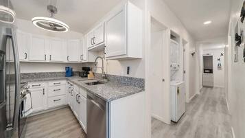Una cocina moderna con armarios blancos, encimera de granito, electrodomésticos de acero inoxidable y lavavajillas integrado.