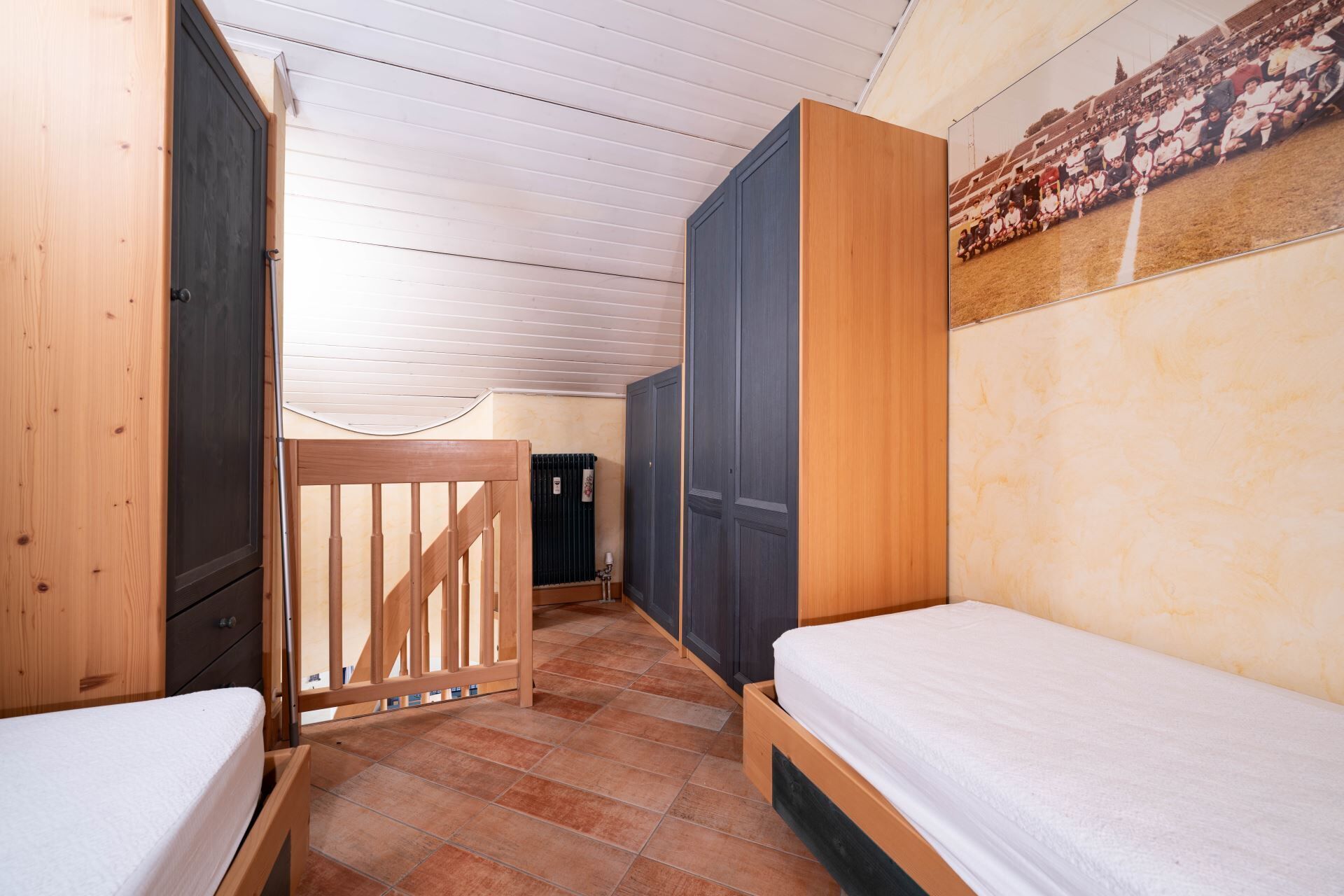 Une petite chambre compacte avec deux lits simples, une armoire en bois et un radiateur.