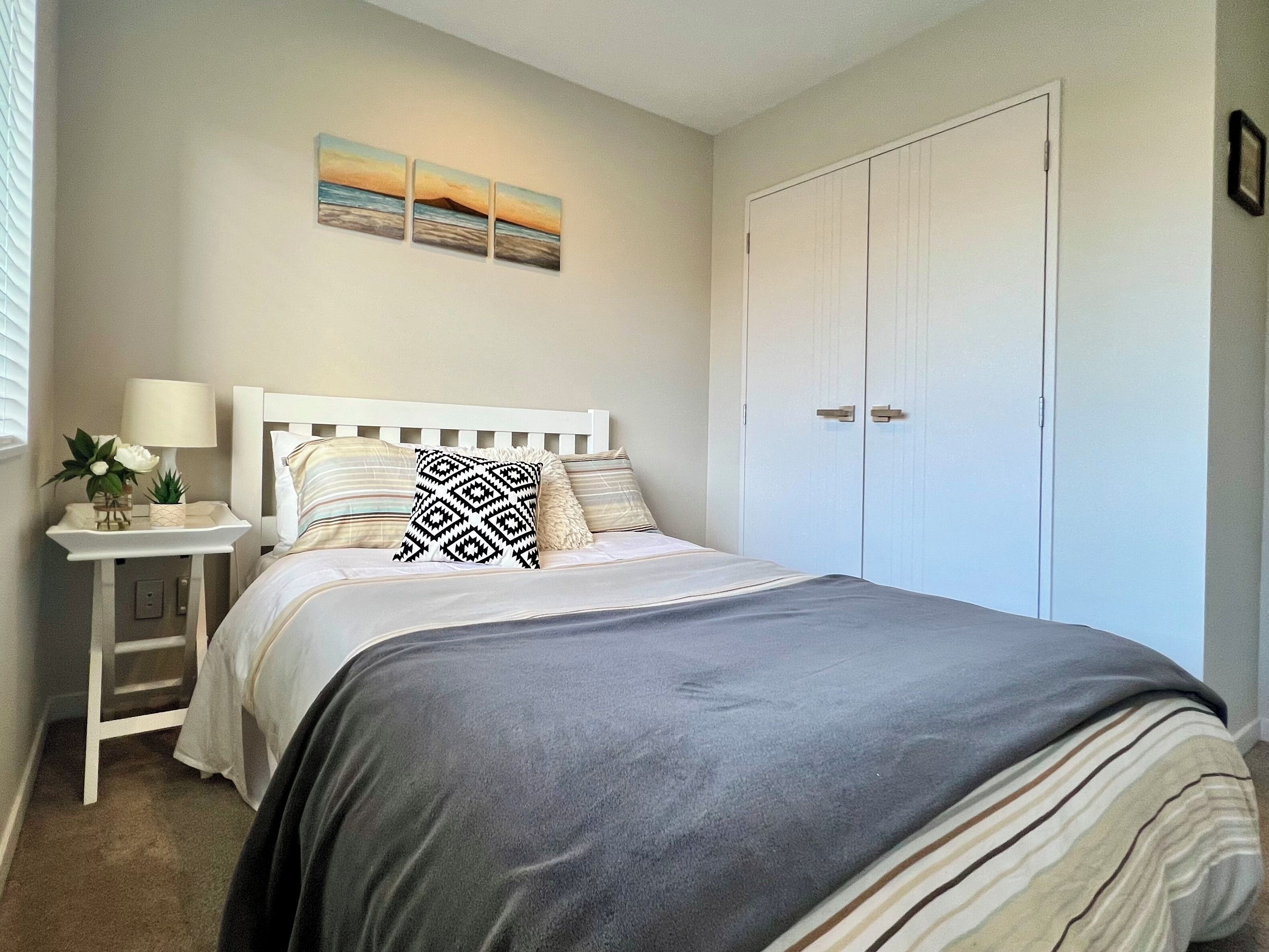 A bedroom with a bed, bedside table, lamp, and a wall-mounted artwork.