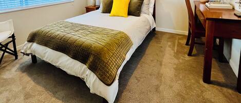 A neatly arranged bedroom with a bed, a desk, and a chair.