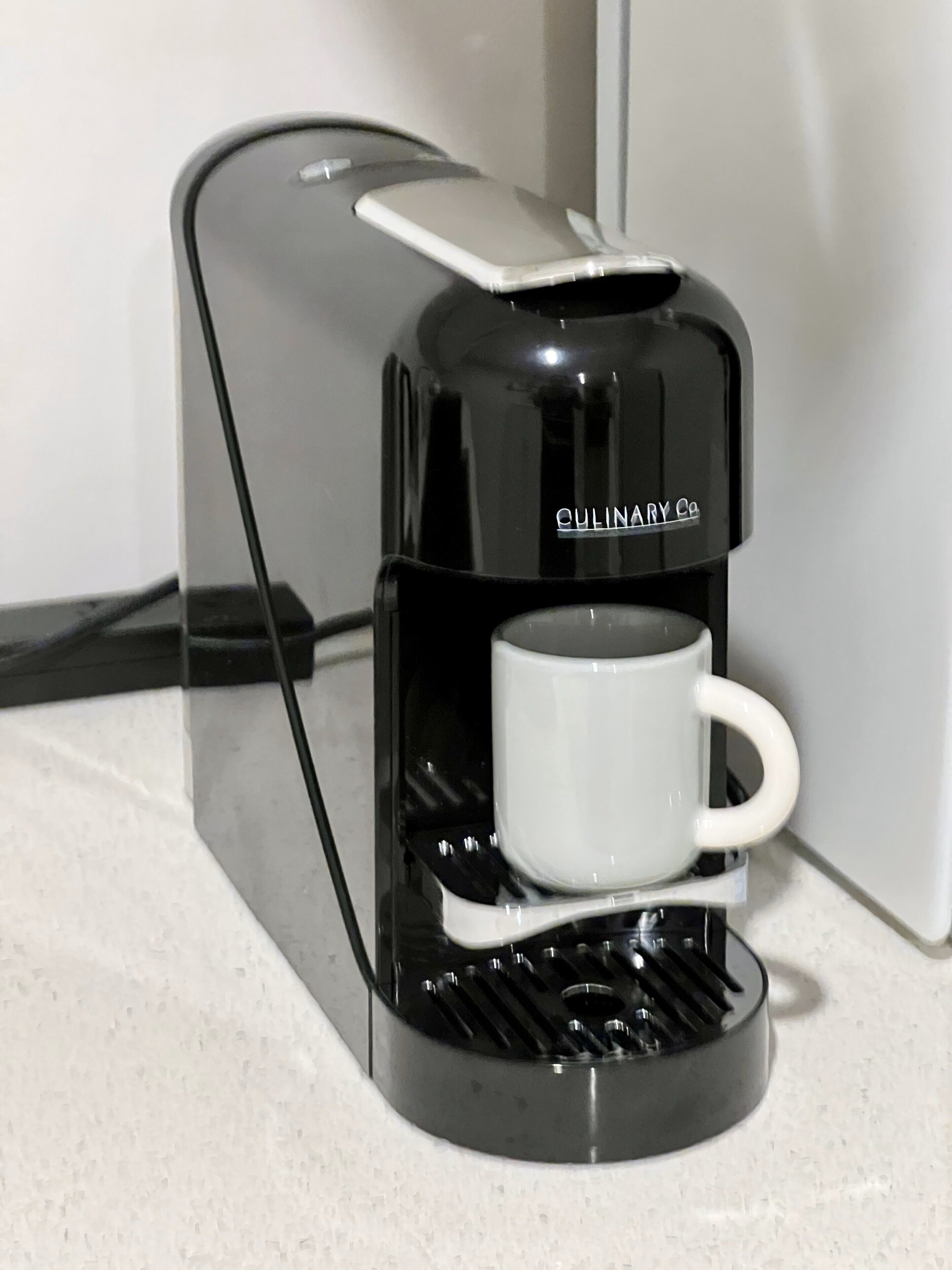 Una cafetera negra con una taza blanca sobre una encimera.