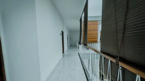 Een gang met witte muren en een marmeren vloer, die uitkomt op een balkon met een houten vloer en uitzicht op de lucht.