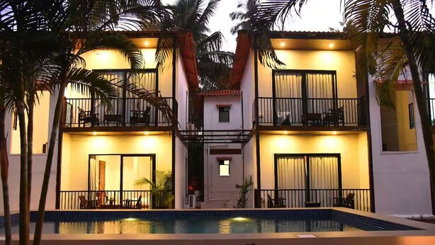A multi-story hotel with a swimming pool, balconies, and palm trees. - Executive room in Arambol near Beach (Arambol)