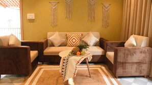 A living room with a sofa, two armchairs, a coffee table with fruit, and macramé wall hangings. - Executive room in Arambol near Beach (Arambol)