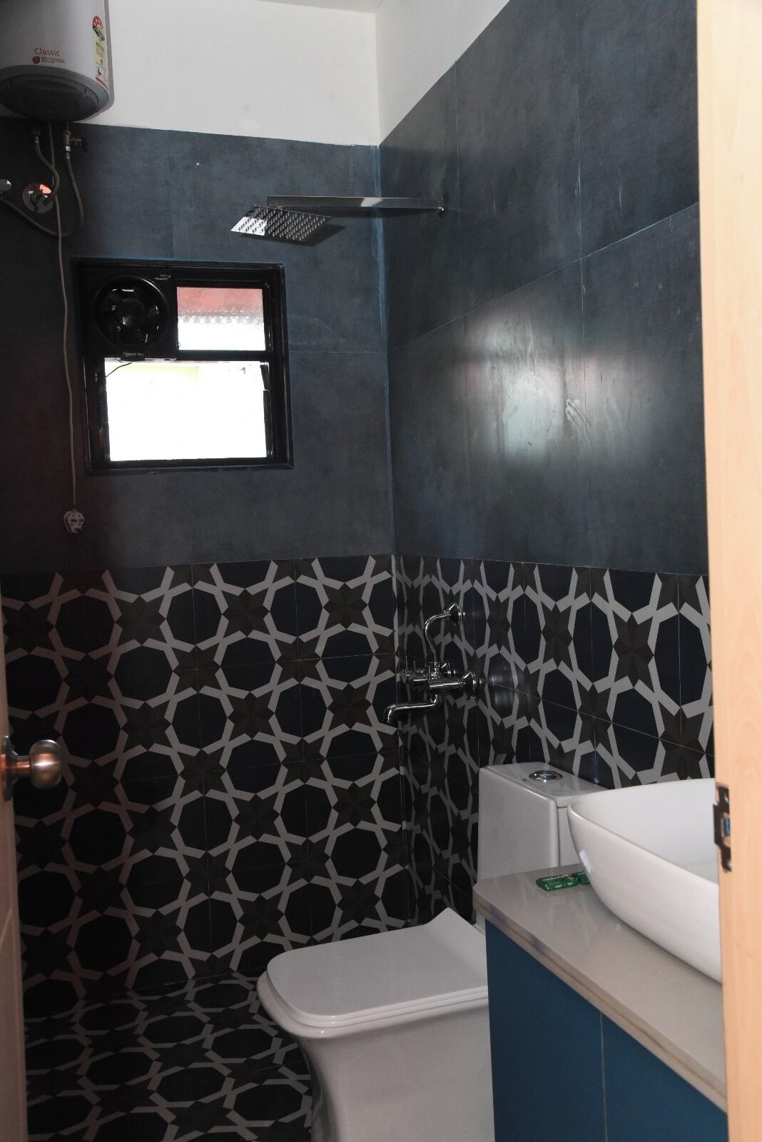 Um banheiro com padrão geométrico em tons de preto e branco, vaso sanitário branco, pia branca e chuveiro com chuveiro de teto preto.