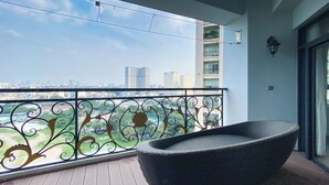 Ein Balkon mit einem Korbstuhl, einem Metallgeländer mit Verzierungen und Blick auf eine Stadtlandschaft.