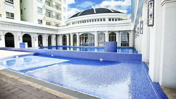 Ein Swimmingpool mit blauem Mosaikmuster, umgeben von einem weißen Gebäude mit Rundbogenfenstern und einer gewölbten Dachform.
