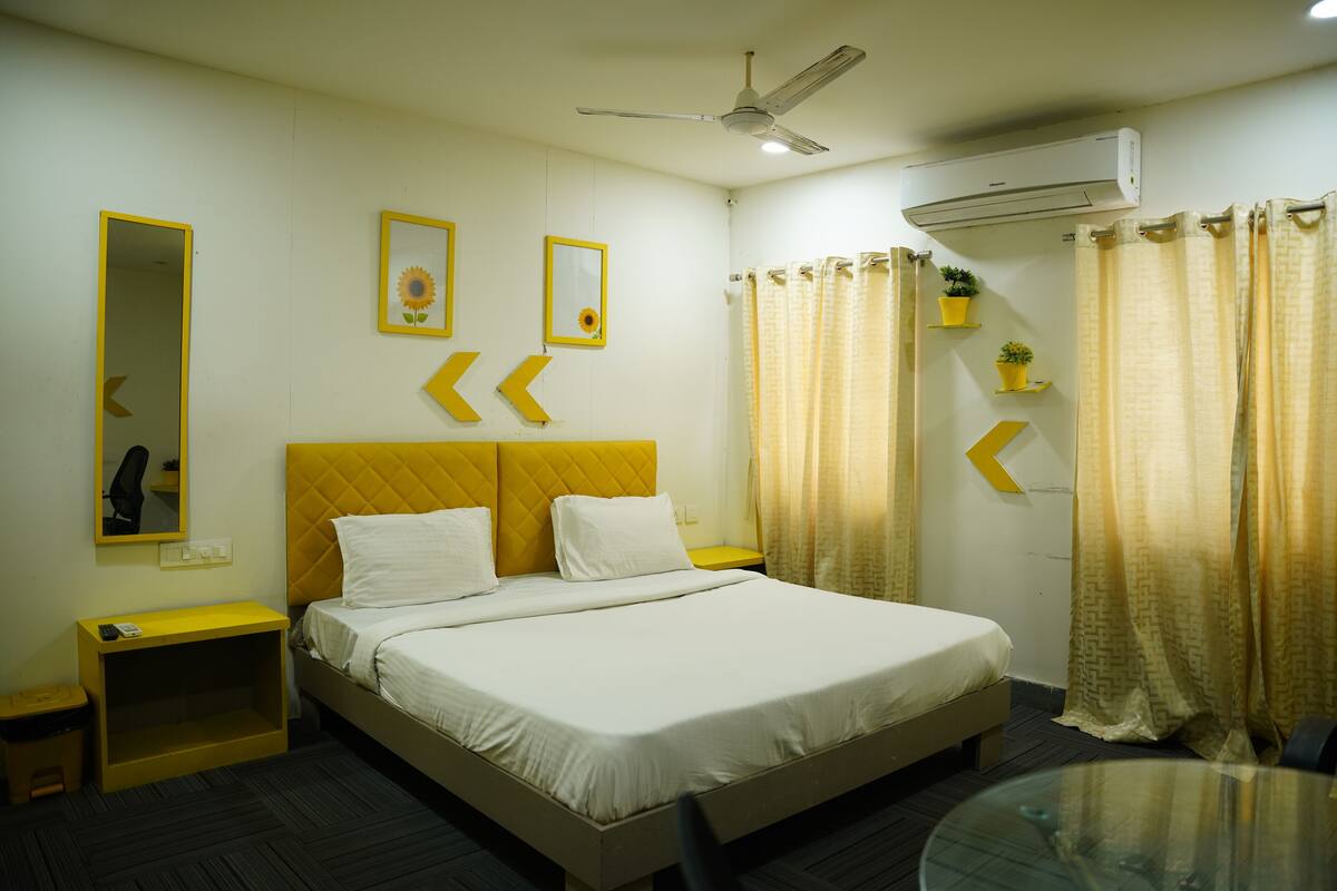 Quarto de hotel com uma cama, mesa de cabeceira, espelho e ventoinha no teto.