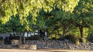 A stone wall, a covered seating area, and a building with a roof. - Petra Olive 1 (Yallingup)