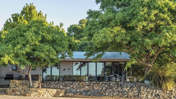 A modern building with a stone wall, outdoor seating, and large windows. - Petra Olive 1 (Yallingup)