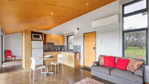 A modern kitchen with a dining area, a sofa with red cushions, and a large window. - Petra Olive 1 (Yallingup)