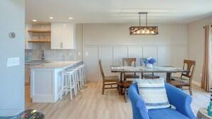 A modern kitchen with white cabinetry, a central island, and bar stools. There is a dining area with a wooden table and chairs, and a blue sofa with a patterned throw. - Oceanfront!  Newly renovated, 4 bd/3 bath, dog friendly, FAST-Wifi and Roku streaming! (North Topsail Beach)