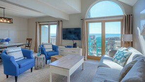 A spacious living room with a large TV, blue and white furniture, a wooden coffee table, and a view of the ocean through large windows. - Oceanfront!  Newly renovated, 4 bd/3 bath, dog friendly, FAST-Wifi and Roku streaming! (North Topsail Beach)