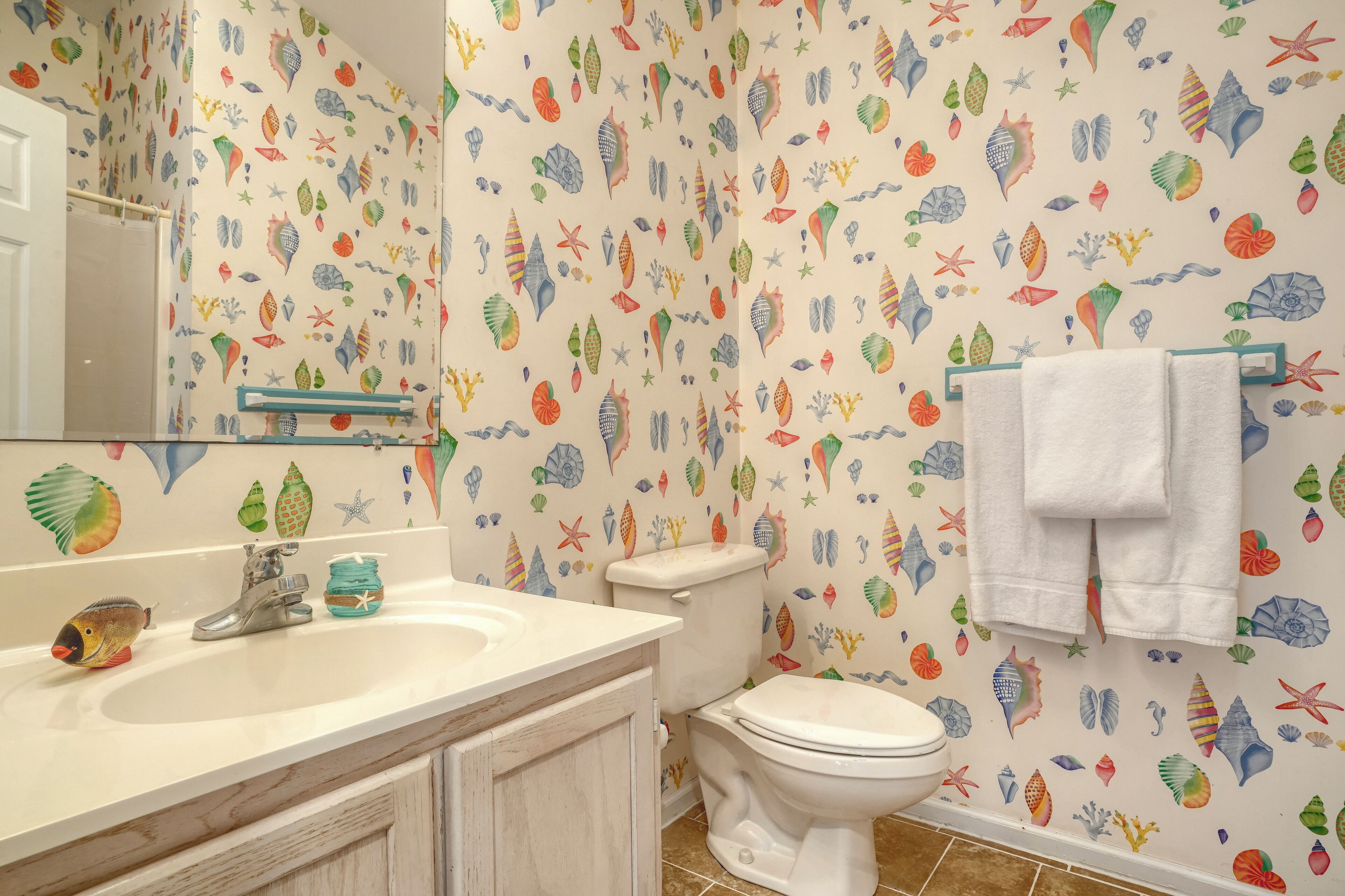 A bathroom with a sink, mirror, and toilet. The walls are decorated with colorful sea creature decals.