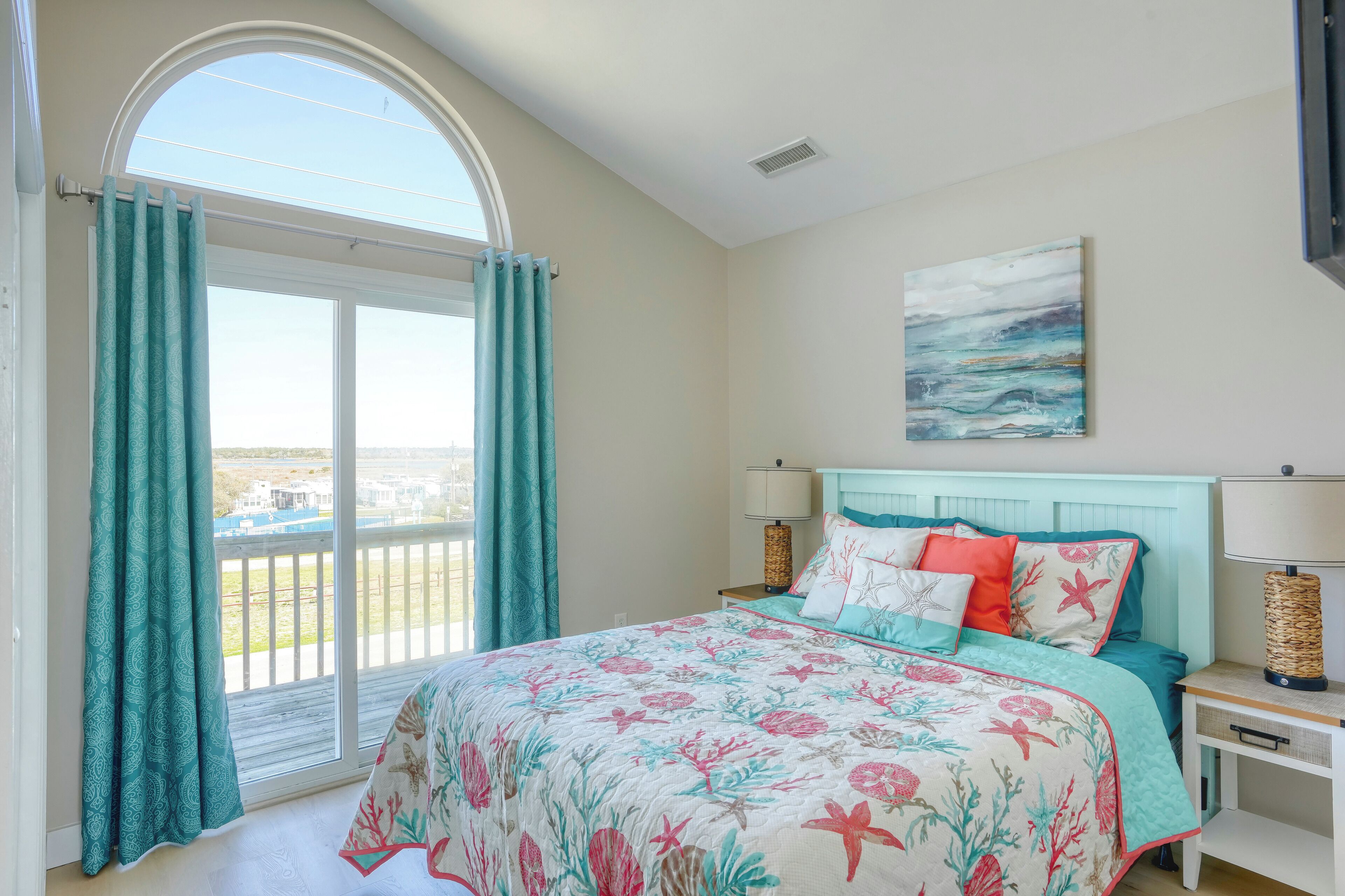 A bedroom with a large bed, a balcony view, and a painting on the wall.