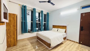 A bedroom with a bed, a ceiling fan, a window with curtains, and a wooden door. - I-ROOMZ S S V Hotel (Hoskote)
