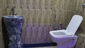 A bathroom with a marble wall, a sink with a unique design, and a toilet with a lid. - I-ROOMZ S S V Hotel (Hoskote)