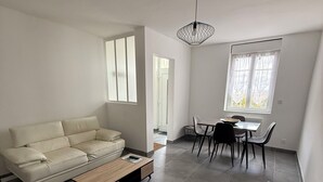 Un soggiorno moderno con divano, tavolino, tavolo da pranzo e sedie. Si vede una finestra con tende e un lampadario.