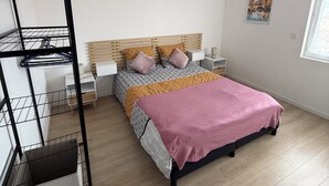 Una camera da letto con un letto, un mobiletto portaoggetti in metallo nero, un comodino, una lampada a parete e un poster appeso al muro.