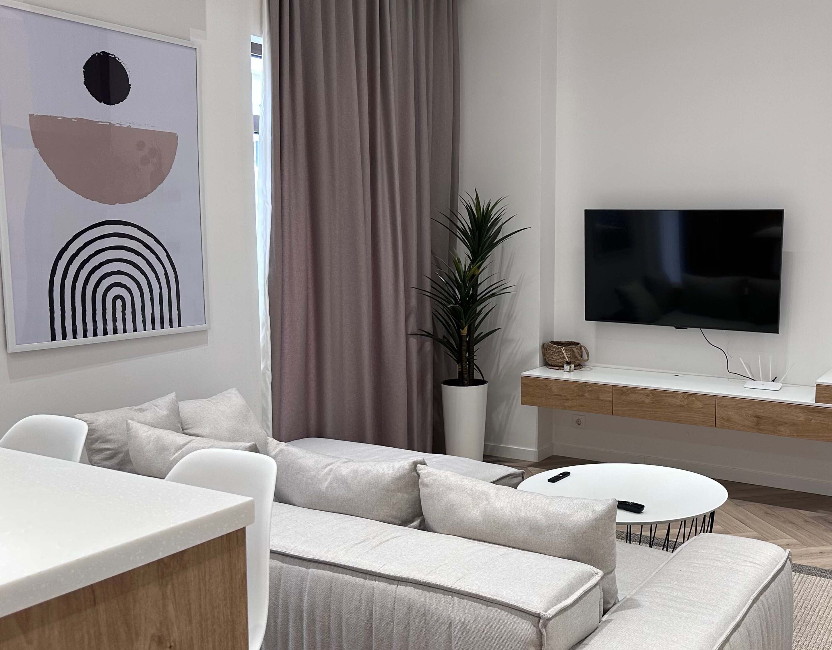 Un soggiorno moderno con un divano bianco, un tavolo da pranzo e una televisione a schermo piatto fissata al muro.
