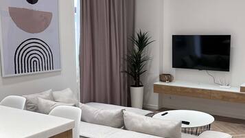 Un soggiorno moderno con un divano bianco, un tavolo da pranzo e una televisione a schermo piatto fissata al muro.