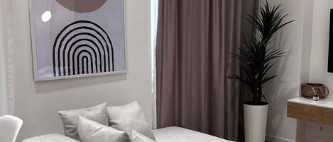 Una sala de estar moderna con un sofá seccional gris, sillas blancas, una mesa de centro redonda, una planta grande en maceta y una obra de arte minimalista en la pared.