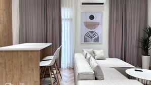 A modern guest room with a wooden accent wall, a white sofa, a small dining area, and a large window with curtains. - Boulevard 46 (Tashkent)