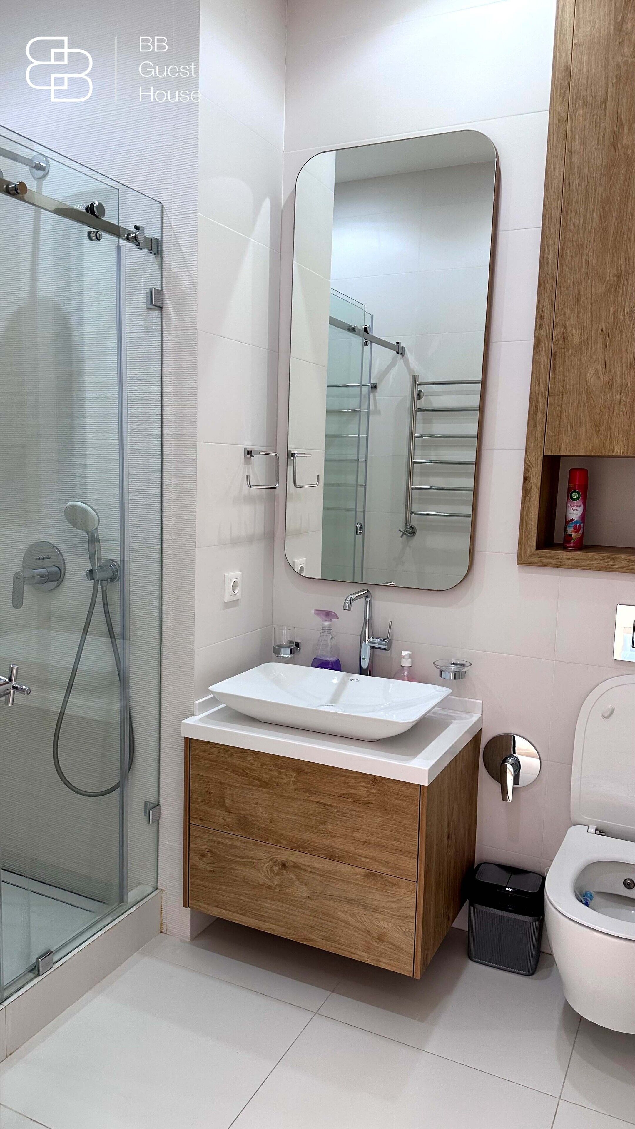 Un baño moderno con ducha envuelta en vidrio, tocador de madera con lavamanos blanco y un espejo grande.