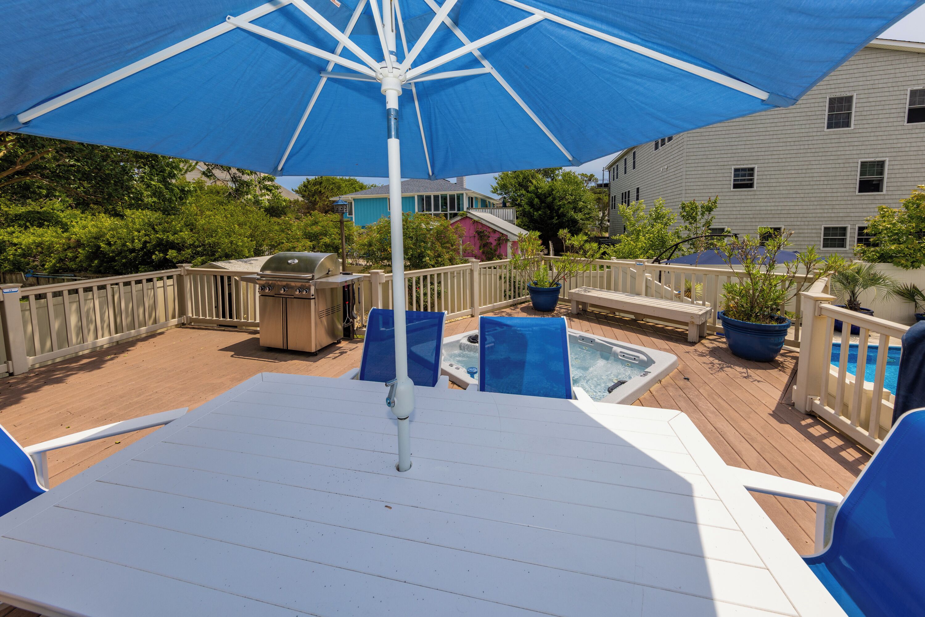 A deck with a white table, blue chairs, a hot tub, and a blue umbrella.