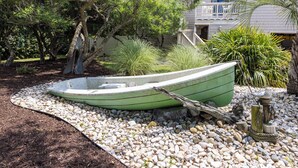 A green boat in a garden with a white fence, surrounded by pebbles and plants. - Rusty Dolphin is a well-maintained 2 level home with pool and hot tub. (Virginia Beach)