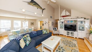 A living room with a sectional sofa, a coffee table, a TV, and a decorative sailboat on the wall. - Rusty Dolphin is a well-maintained 2 level home with pool and hot tub. (Virginia Beach)