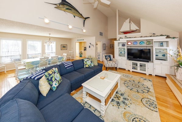 A living room with a sectional sofa, a coffee table, a TV, and a decorative sailboat on the wall.