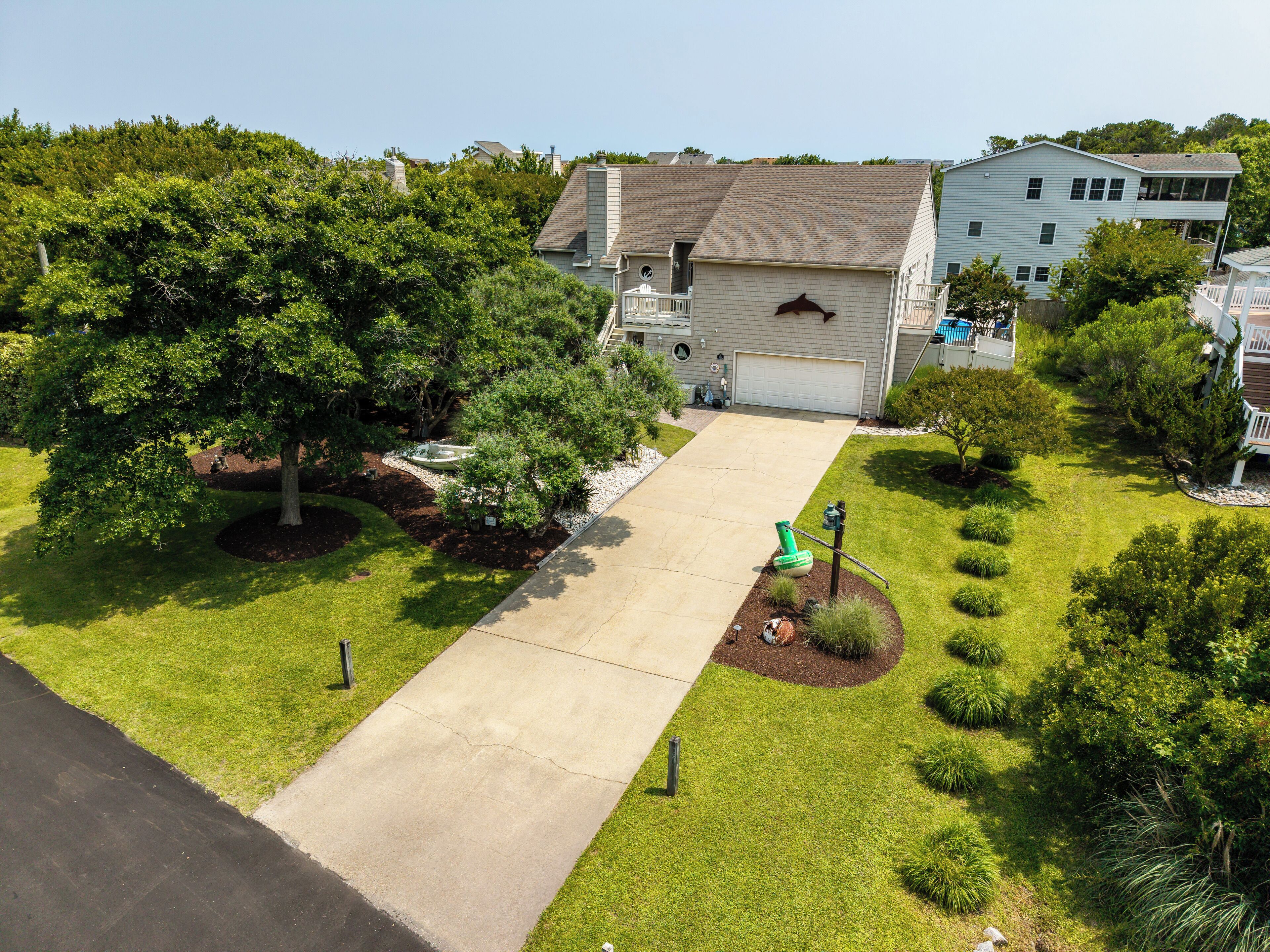 A residential driveway leading to a house with a garage, surrounded by well-maintained lawns and trees.