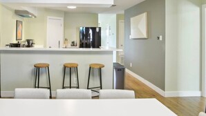 A modern kitchen with a white countertop, three stools, and a stainless steel refrigerator.