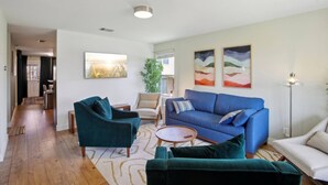 A modern living room with a blue sofa, teal armchairs, and a coffee table. There are two abstract paintings on the wall and a potted plant.