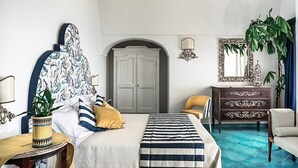 A bedroom with a bed, a dresser, a chair, a potted plant, and a mirror.
