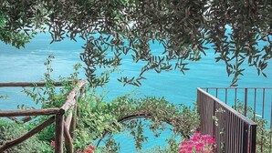 A stone staircase leading to a balcony overlooking a body of water, with a wooden railing and potted plants.