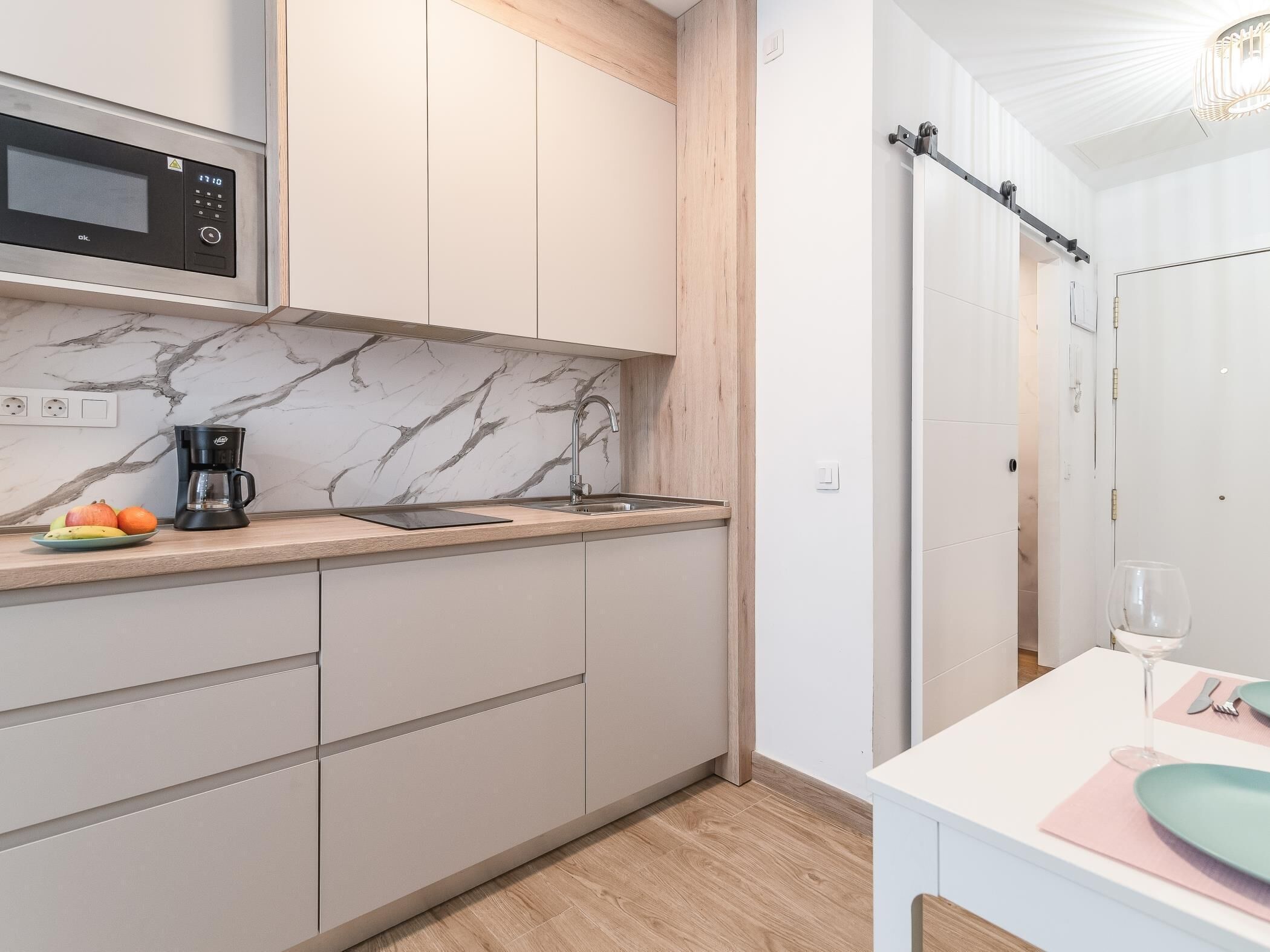A modern kitchen with a built-in microwave, a coffee maker, and a marble backsplash.
