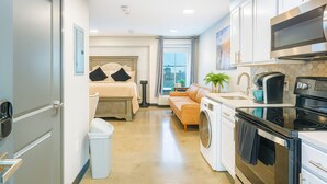 A compact hotel room with a bed, a sofa, a washing machine, a microwave, and a sink.