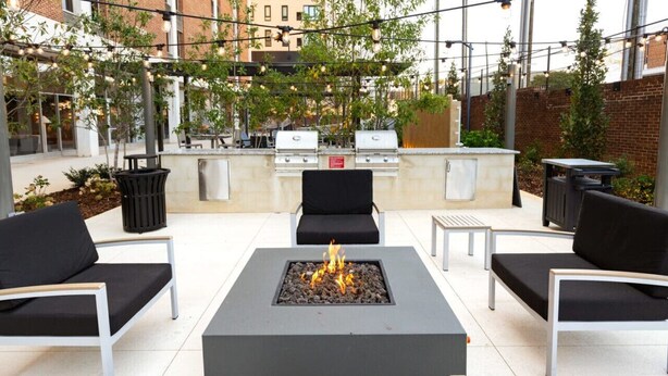 An outdoor patio with a central fire feature, seating, and a grill area.