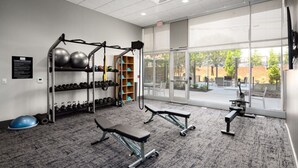 A gym with exercise equipment, a wall-mounted rack with dumbbells, and a large window with a view of the outdoors.